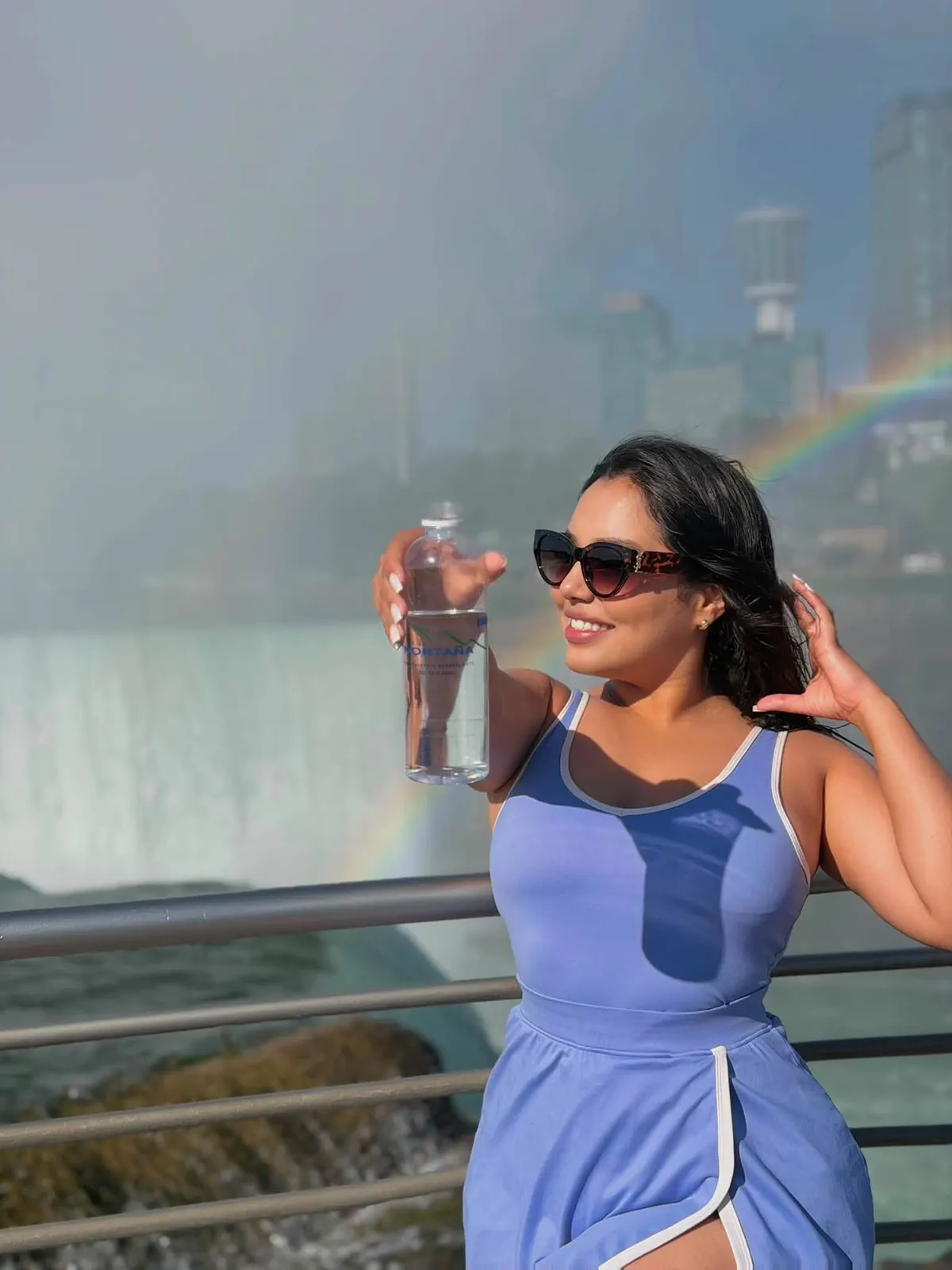 Una mujer levanta una botella de 500 ml de Agua de la Montaña frente a una cascada